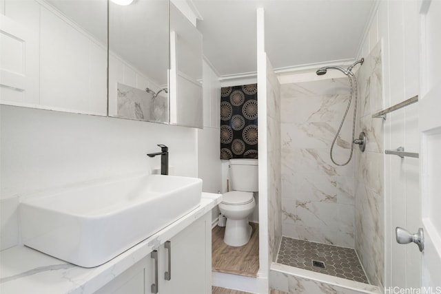 bathroom with vanity, hardwood / wood-style flooring, toilet, ornamental molding, and a tile shower