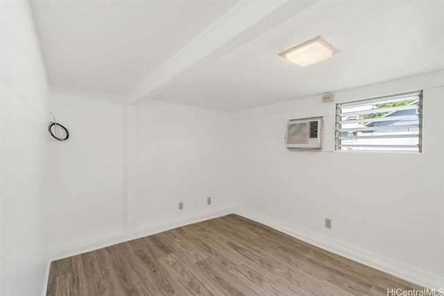 spare room featuring wood-type flooring, an AC wall unit, and beam ceiling