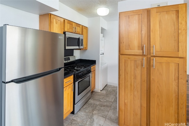 kitchen with appliances with stainless steel finishes, a textured ceiling, and stacked washing maching and dryer