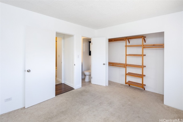 unfurnished bedroom with connected bathroom, light carpet, a textured ceiling, and a closet