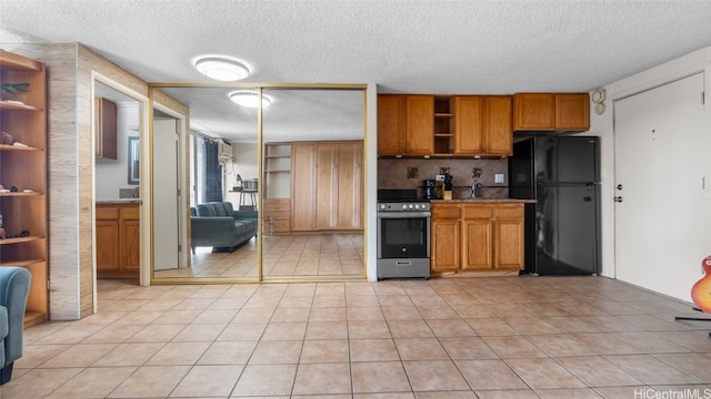 kitchen with stainless steel range oven, a textured ceiling, decorative backsplash, light tile patterned floors, and black refrigerator