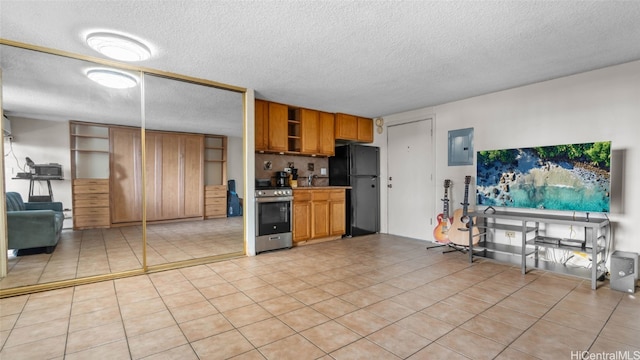 kitchen with stainless steel range oven, a textured ceiling, electric panel, black fridge, and light tile patterned floors