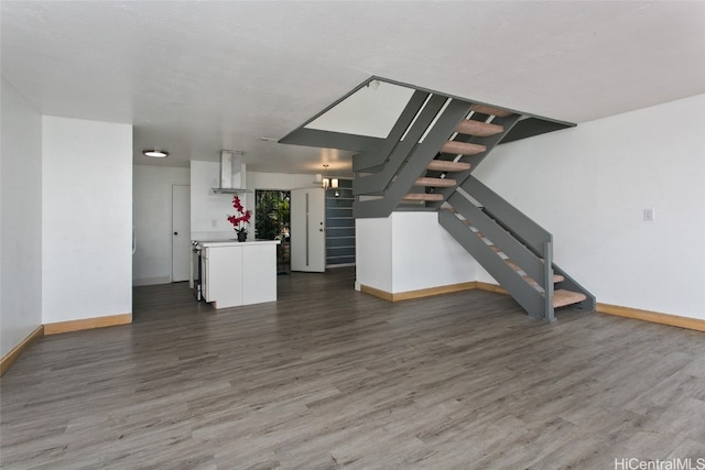 unfurnished living room with wood finished floors, baseboards, and stairs