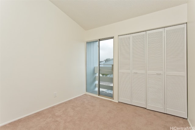 unfurnished bedroom with carpet, a closet, lofted ceiling, and baseboards