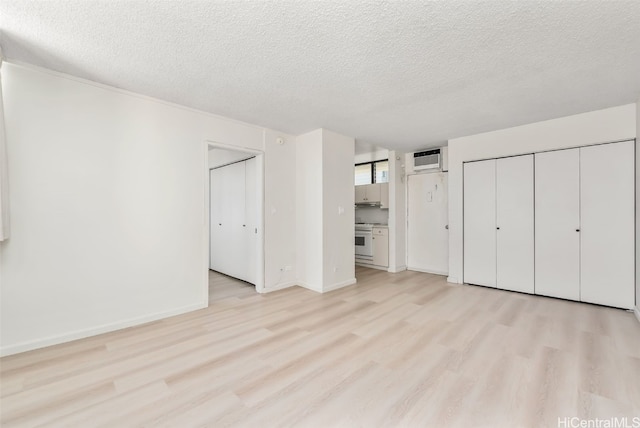 unfurnished bedroom with multiple closets, a wall mounted AC, a textured ceiling, and light hardwood / wood-style floors