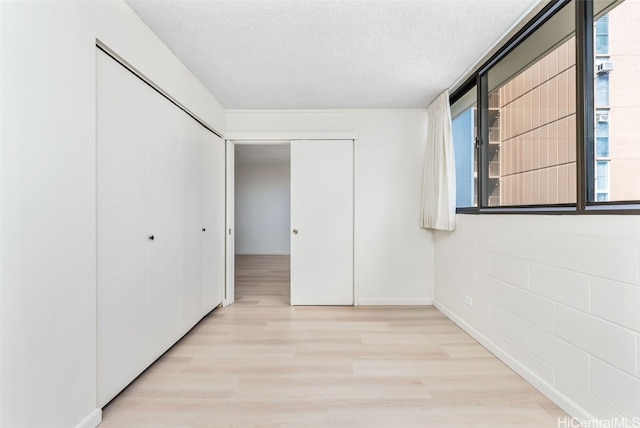 unfurnished bedroom featuring light hardwood / wood-style flooring, a textured ceiling, and a closet