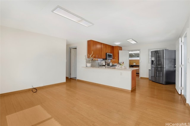 kitchen featuring kitchen peninsula, light hardwood / wood-style floors, decorative backsplash, and appliances with stainless steel finishes