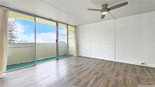 empty room with expansive windows, hardwood / wood-style flooring, plenty of natural light, and ceiling fan