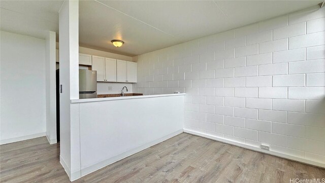 kitchen with white cabinetry, sink, light hardwood / wood-style flooring, kitchen peninsula, and stainless steel fridge