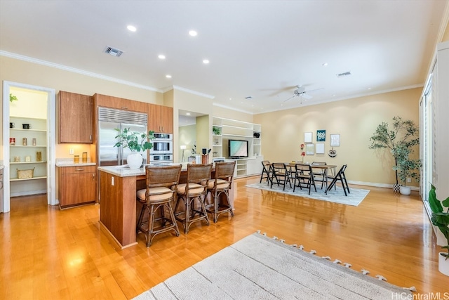 kitchen with appliances with stainless steel finishes, ornamental molding, a kitchen island, and light hardwood / wood-style floors