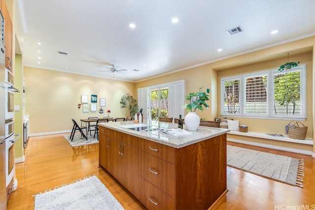 kitchen featuring light hardwood / wood-style flooring, ornamental molding, a healthy amount of sunlight, and a center island with sink