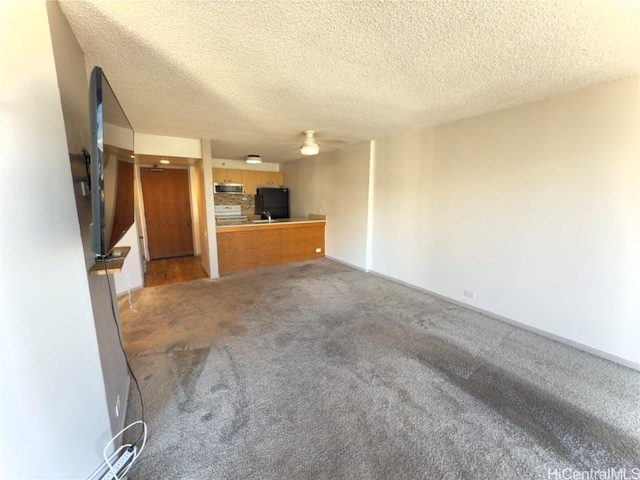 unfurnished living room with a textured ceiling, ceiling fan, carpet, and sink