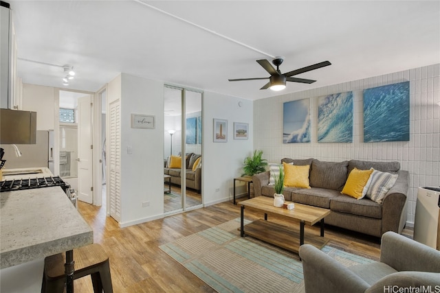 living room featuring tile walls, sink, light wood-type flooring, and ceiling fan