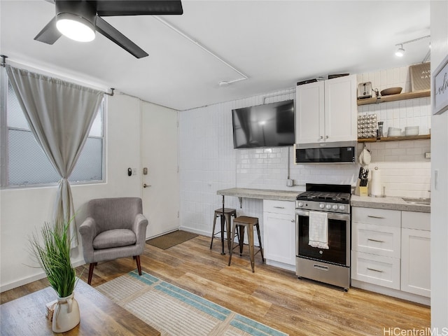 kitchen with appliances with stainless steel finishes, backsplash, a kitchen breakfast bar, light hardwood / wood-style floors, and white cabinets