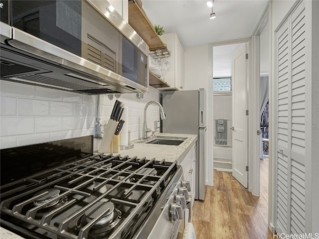 kitchen featuring tasteful backsplash, light stone countertops, sink, light hardwood / wood-style floors, and stainless steel appliances