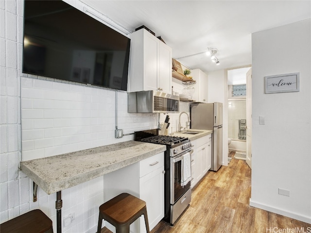 kitchen with a kitchen breakfast bar, white cabinets, light hardwood / wood-style flooring, and stainless steel appliances