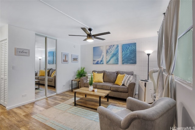 living room featuring light hardwood / wood-style floors, tile walls, and ceiling fan