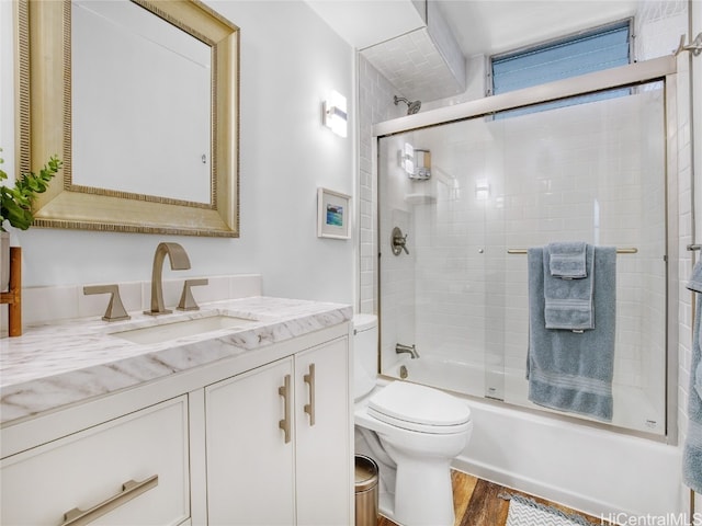 full bathroom featuring vanity, toilet, combined bath / shower with glass door, and hardwood / wood-style floors