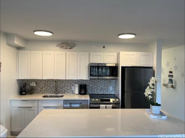 kitchen with tasteful backsplash, appliances with stainless steel finishes, sink, and white cabinets