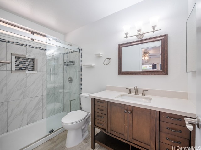 bathroom with wood-type flooring, a shower with shower door, toilet, ceiling fan, and vanity