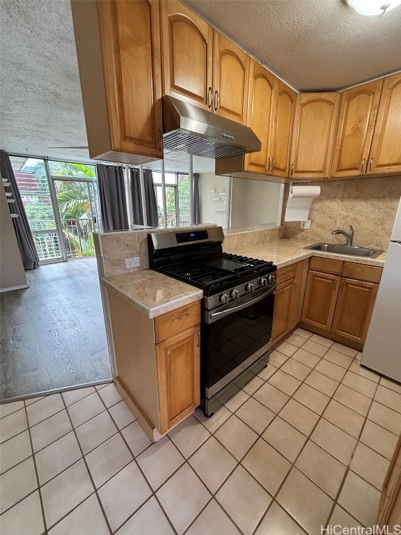 kitchen with light tile patterned floors, a textured ceiling, white fridge, sink, and stainless steel gas range