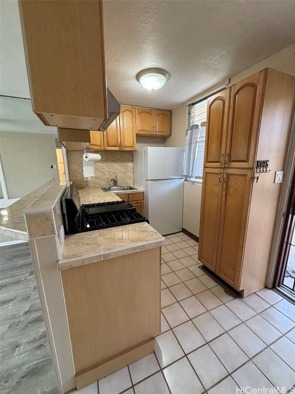 kitchen featuring sink, a textured ceiling, kitchen peninsula, stove, and white refrigerator