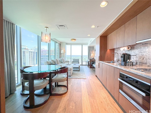 kitchen featuring tasteful backsplash, stovetop, stainless steel oven, light hardwood / wood-style flooring, and decorative light fixtures