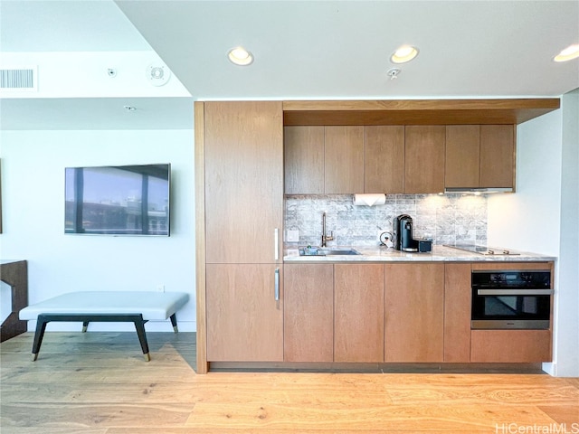 kitchen with decorative backsplash, stainless steel oven, light hardwood / wood-style flooring, ventilation hood, and sink