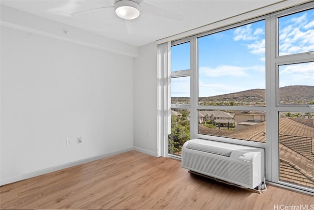 unfurnished room with a mountain view, light hardwood / wood-style floors, an AC wall unit, and ceiling fan