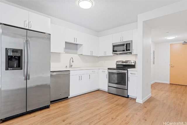 kitchen with appliances with stainless steel finishes, white cabinetry, light hardwood / wood-style flooring, and sink