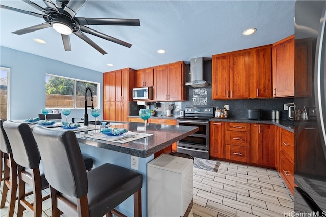 kitchen featuring appliances with stainless steel finishes, wall chimney exhaust hood, a breakfast bar area, backsplash, and an island with sink