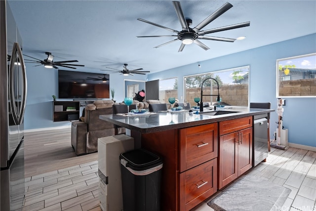 kitchen with stainless steel appliances, sink, light wood-type flooring, and an island with sink