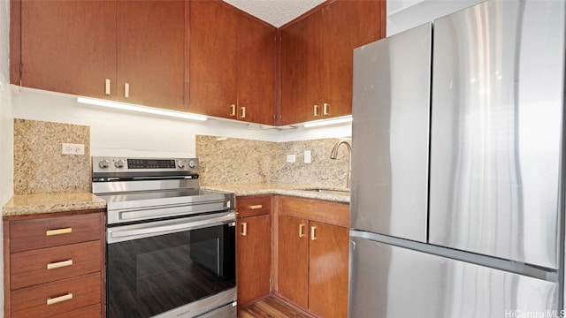 kitchen featuring wood-type flooring, sink, light stone countertops, appliances with stainless steel finishes, and tasteful backsplash