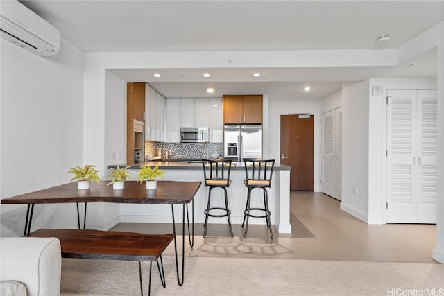 kitchen with white cabinets, a breakfast bar area, tasteful backsplash, appliances with stainless steel finishes, and an AC wall unit