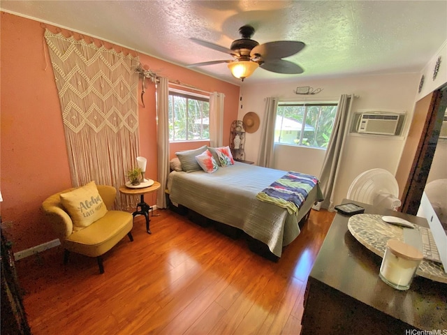 bedroom with light wood finished floors, a textured ceiling, an AC wall unit, and a ceiling fan