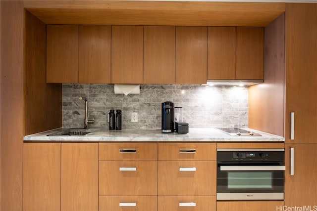 kitchen with sink, backsplash, stainless steel oven, light stone counters, and electric cooktop