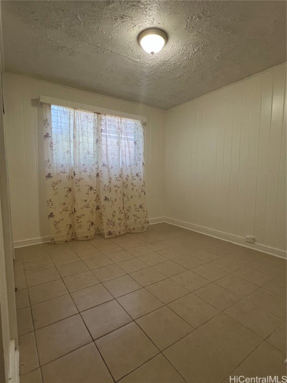 empty room featuring a textured ceiling, wooden walls, and light tile patterned floors