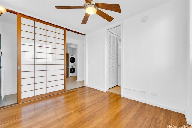 spare room featuring stacked washing maching and dryer, light hardwood / wood-style floors, and ceiling fan