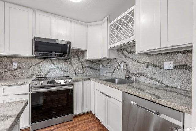 kitchen with a sink, dark wood-style floors, white cabinetry, appliances with stainless steel finishes, and decorative backsplash