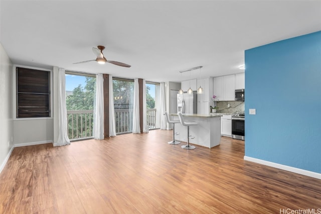 unfurnished living room with a ceiling fan, baseboards, light wood-type flooring, and expansive windows