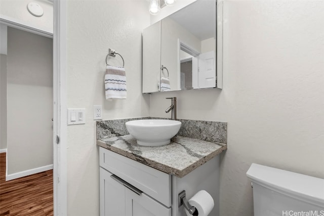 bathroom featuring baseboards, toilet, wood finished floors, and vanity