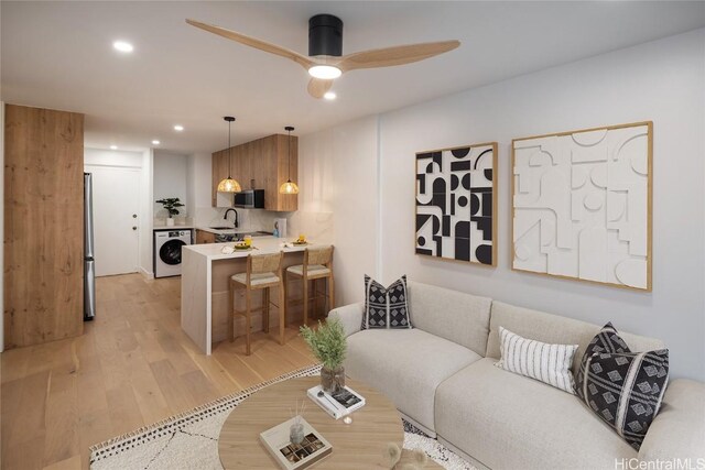 living room with ceiling fan, light wood-type flooring, sink, and washer / clothes dryer