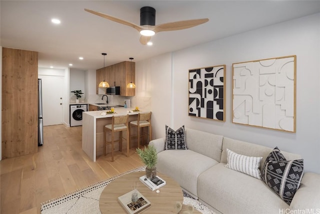 living room featuring ceiling fan, sink, washer / clothes dryer, and light hardwood / wood-style floors