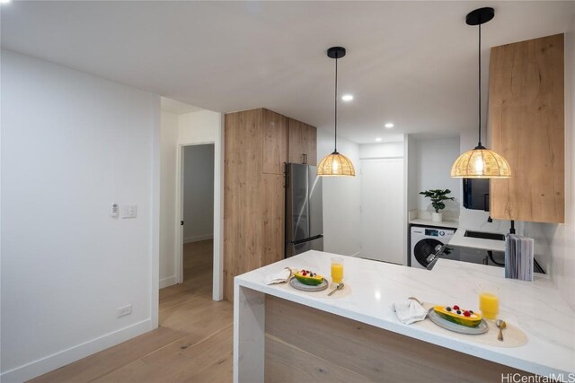 kitchen featuring hanging light fixtures, washer / dryer, kitchen peninsula, and stainless steel refrigerator