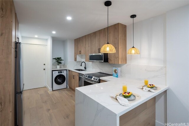 kitchen with light stone counters, kitchen peninsula, pendant lighting, stainless steel appliances, and washer / clothes dryer