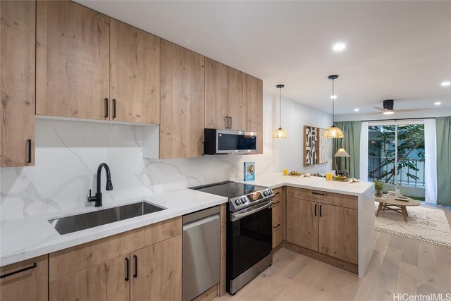 kitchen with sink, appliances with stainless steel finishes, light stone counters, decorative light fixtures, and kitchen peninsula