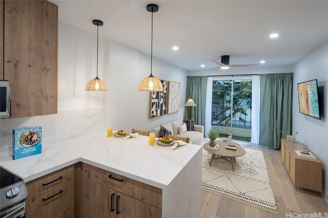 kitchen featuring decorative light fixtures, ceiling fan, stainless steel appliances, light stone countertops, and light wood-type flooring