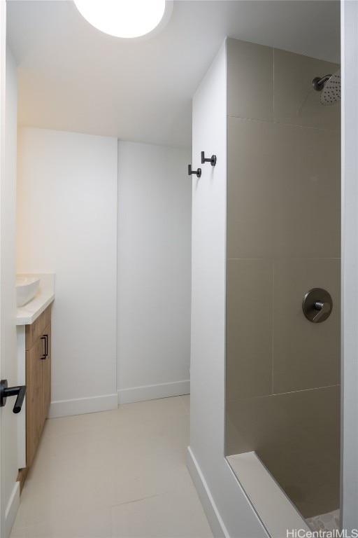 bathroom with tiled shower, vanity, and baseboards