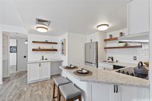 kitchen featuring a kitchen bar, white cabinets, sink, light wood-type flooring, and stainless steel fridge