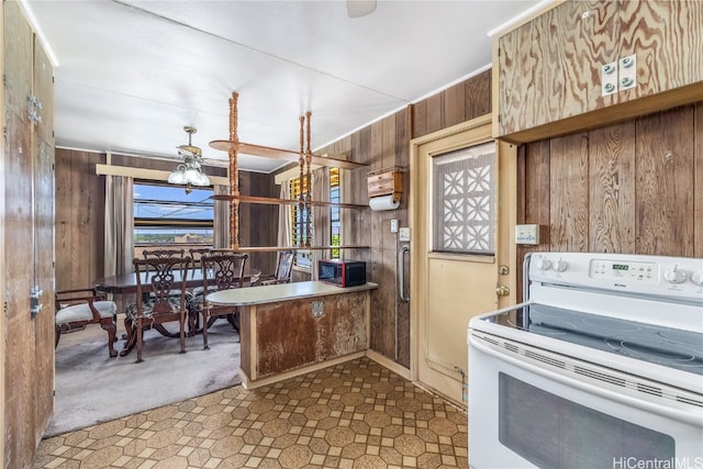 kitchen featuring kitchen peninsula, light carpet, wooden walls, ceiling fan, and white range with electric stovetop